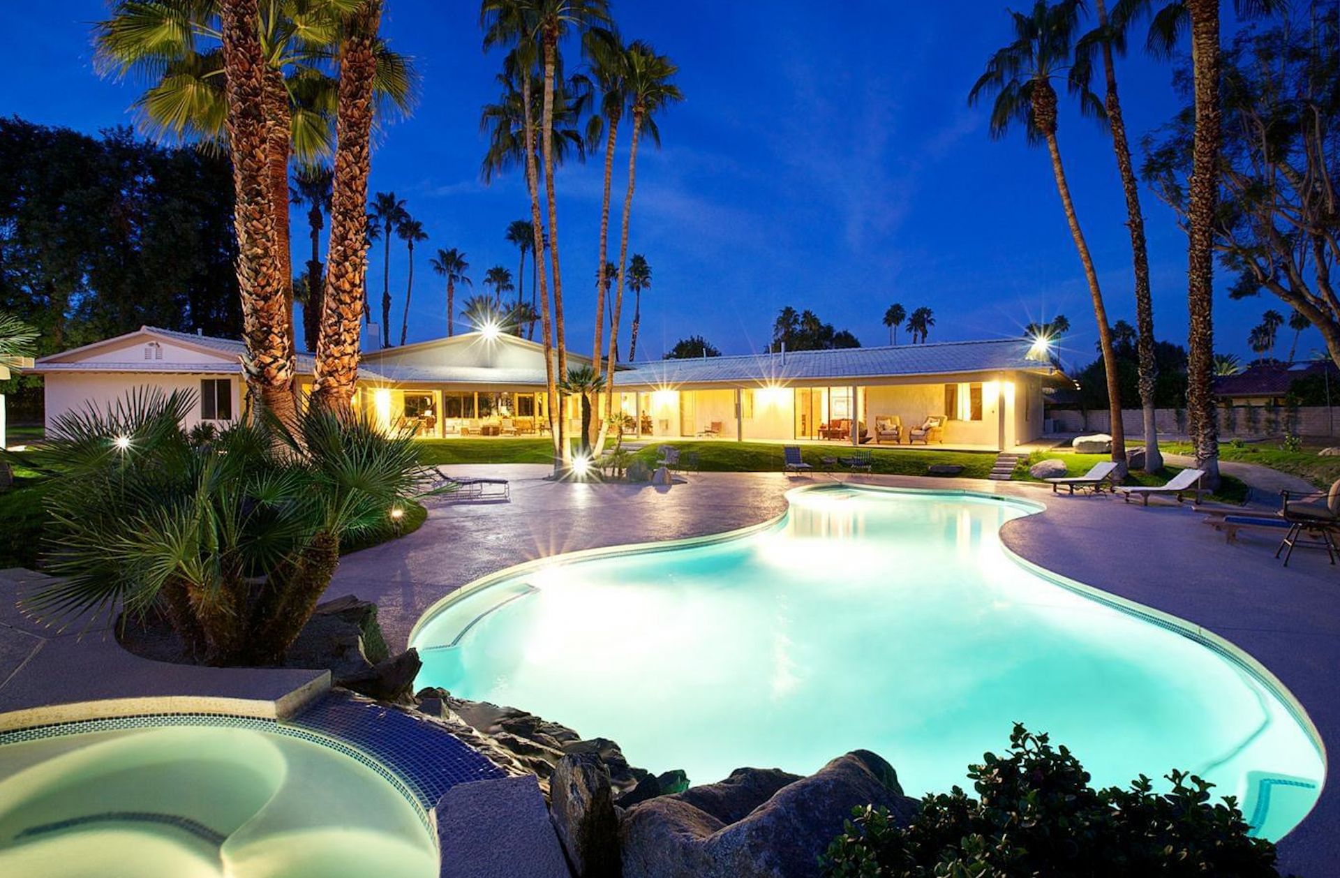 A large swimming pool in front of a house at night