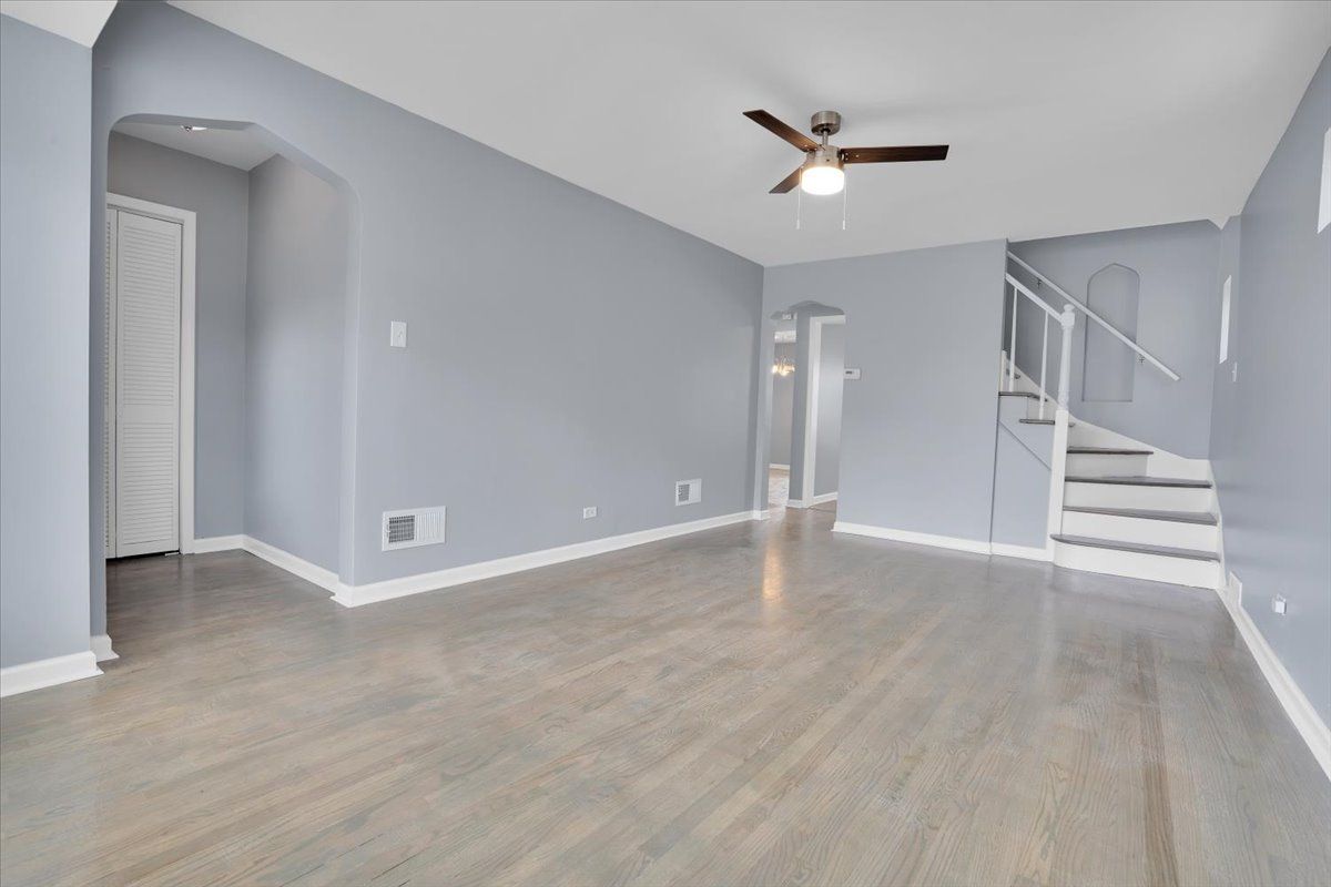 Empty living room with gray walls, hardwood floors, and a ceiling fan.