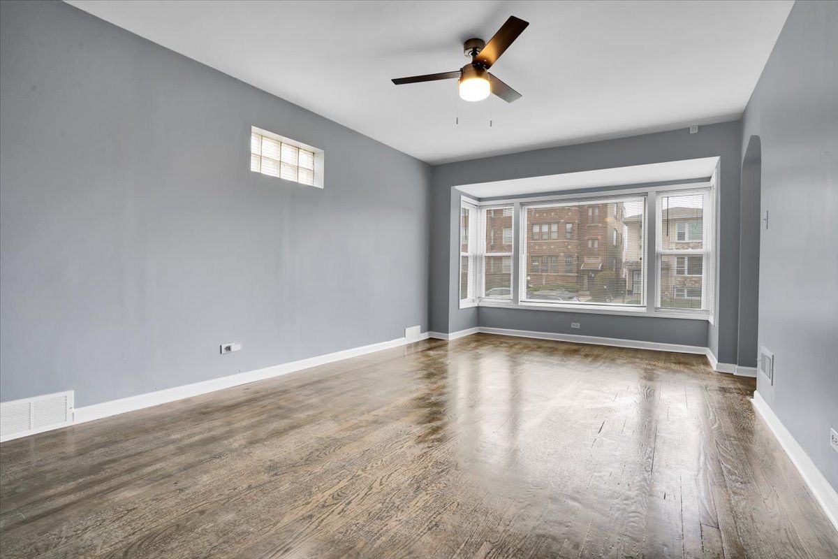 Empty room with gray walls, wood floor, bay window, and ceiling fan.