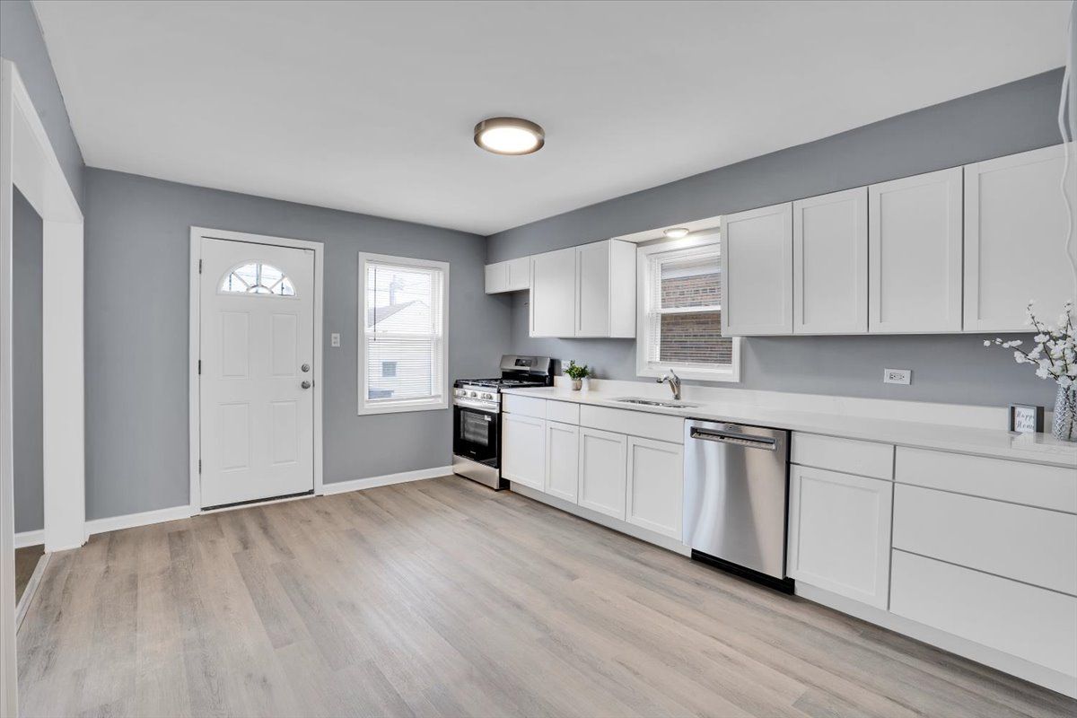 Modern kitchen with white cabinets, stainless steel appliances, and gray walls.