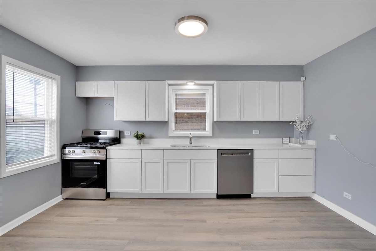 A modern kitchen with white cabinets, stainless steel appliances, and gray walls.