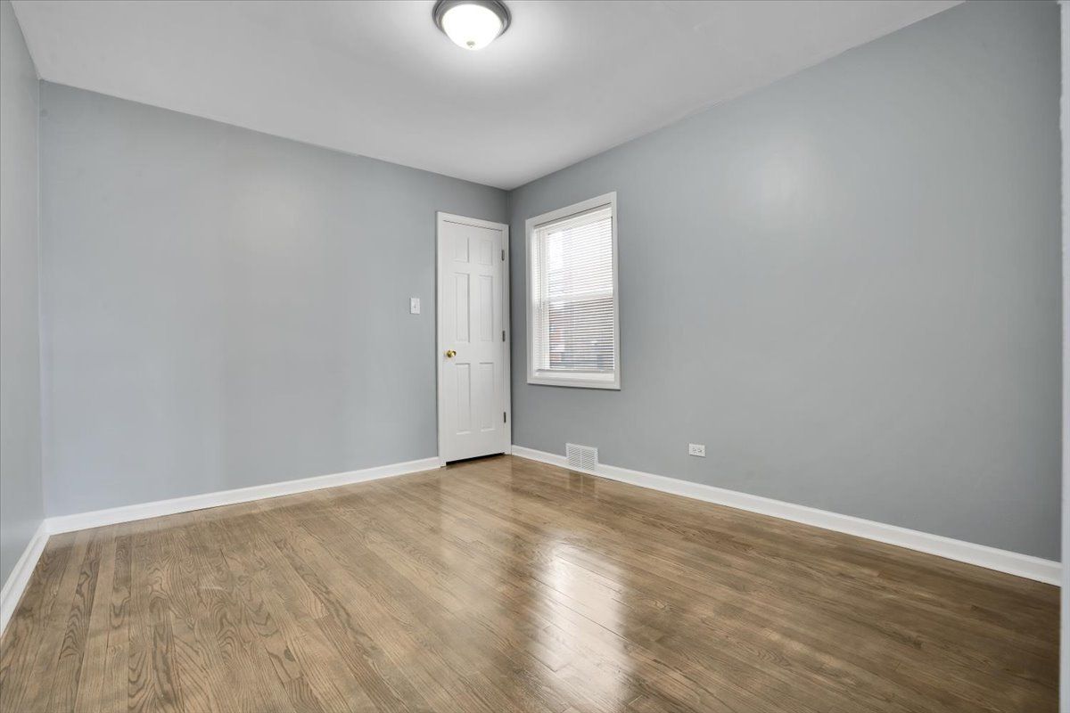 Empty bedroom with light blue walls, white door, window, and hardwood floors.
