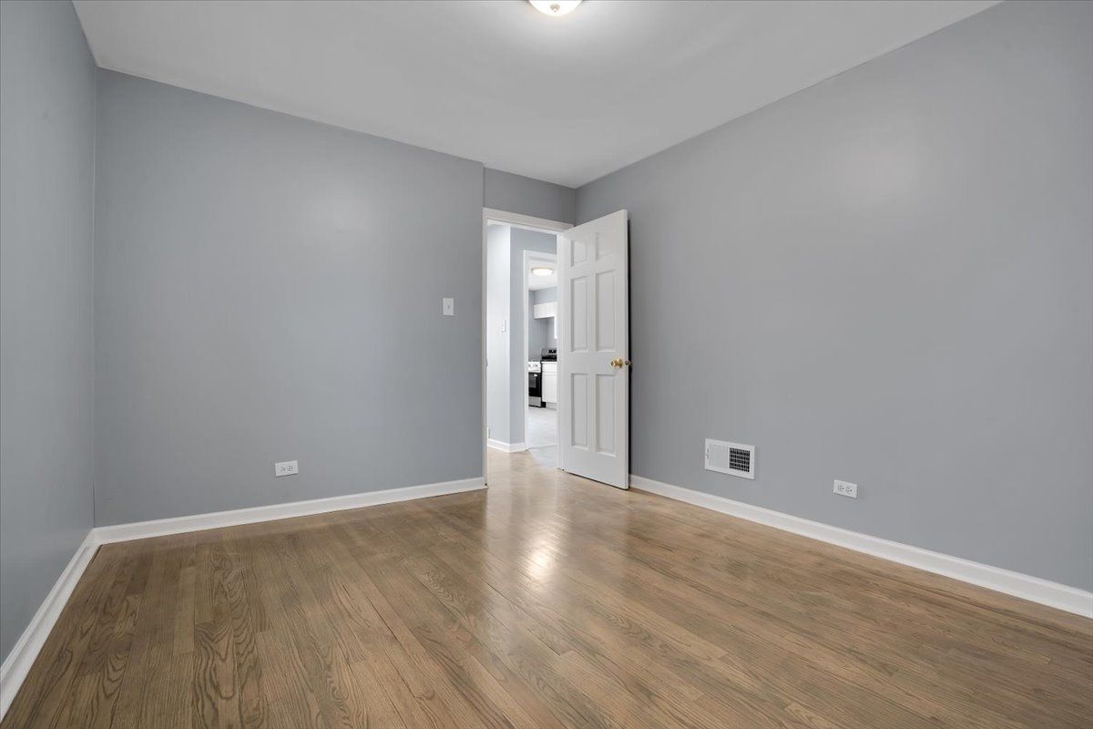Empty room with gray walls, white trim, and wooden floor, with a doorway leading to another room.
