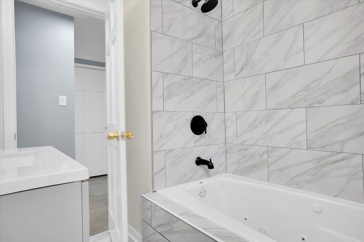 Bathroom with white tub and marble-look tile, black fixtures. Doorway leads to another room.