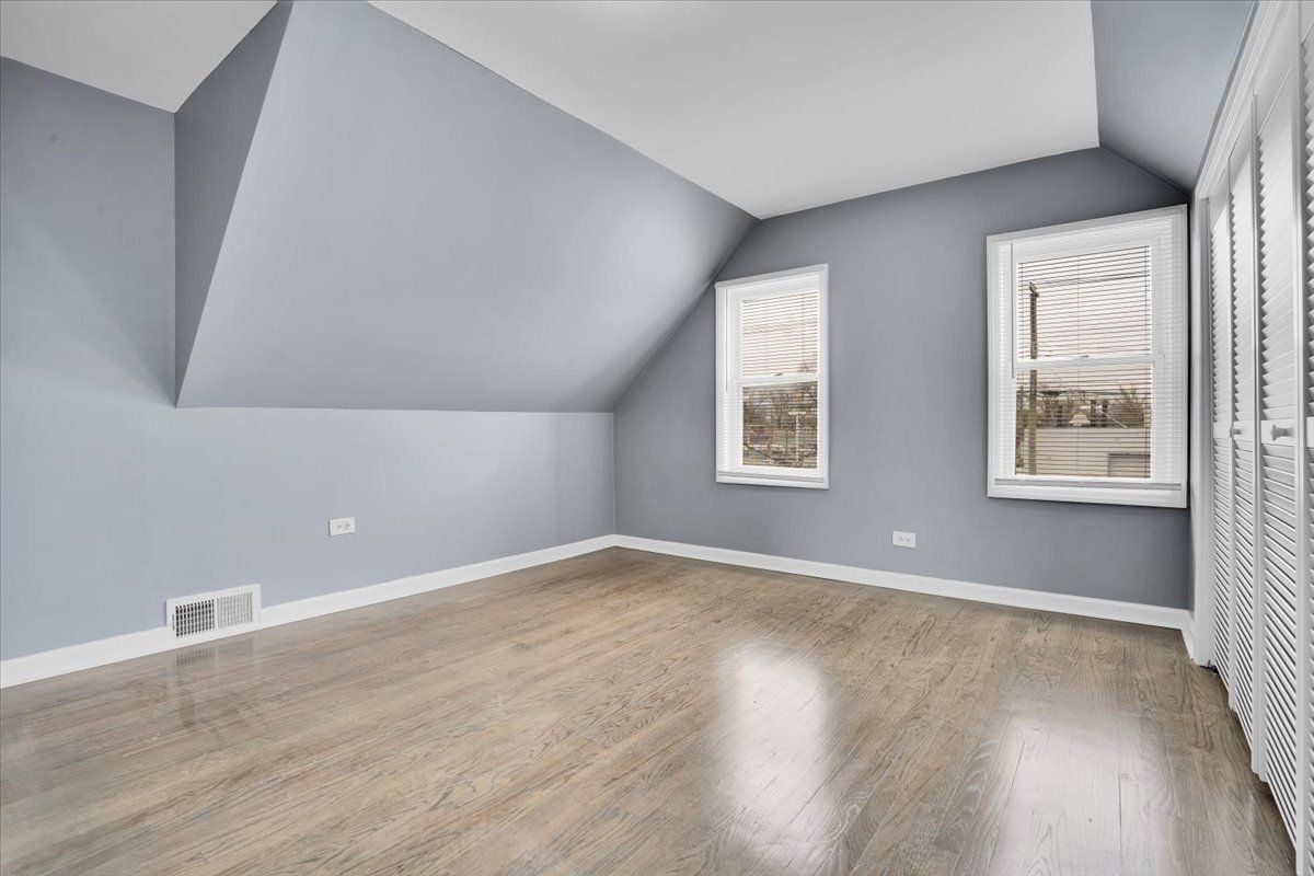 Empty, blue-walled room with hardwood floors, two windows, and a slanted ceiling.