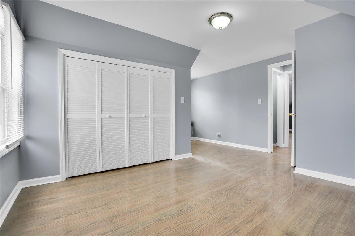 Empty bedroom with light wood floors, white closet doors, and gray walls.
