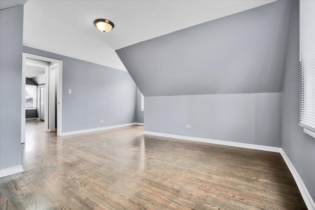 Empty room with angled ceiling, painted light blue, and hardwood floors.