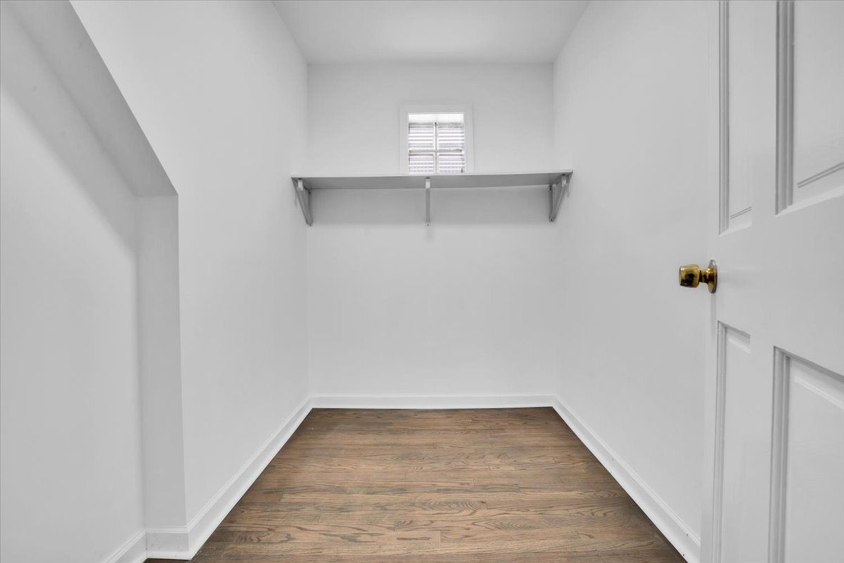 Empty white storage closet with wooden floor, shelf, and door.