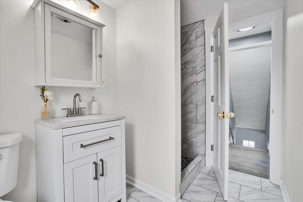 White bathroom with vanity, mirror, and open door to hallway.