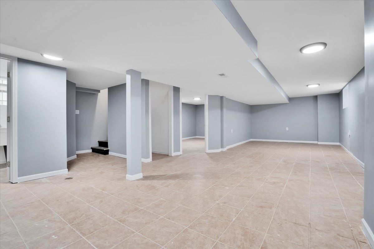 Empty, finished basement with beige flooring, light gray walls, and support pillars.