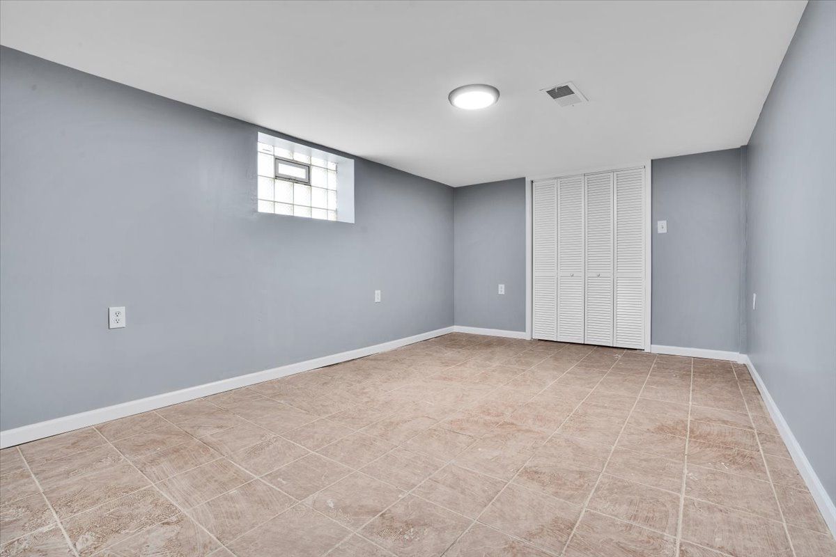 Empty room with gray walls, tan tile floor, small window, and closed white closet doors.