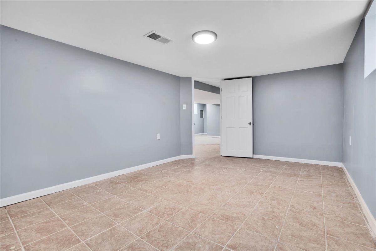Empty room with light blue walls, beige tile floor, and white door.