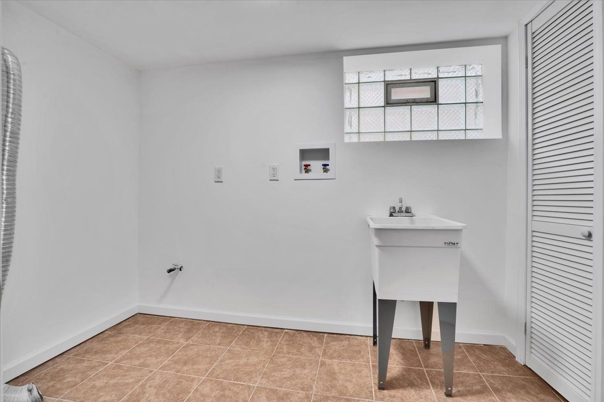 Laundry room with a white sink, window, and door. Beige tiled floor. White walls.