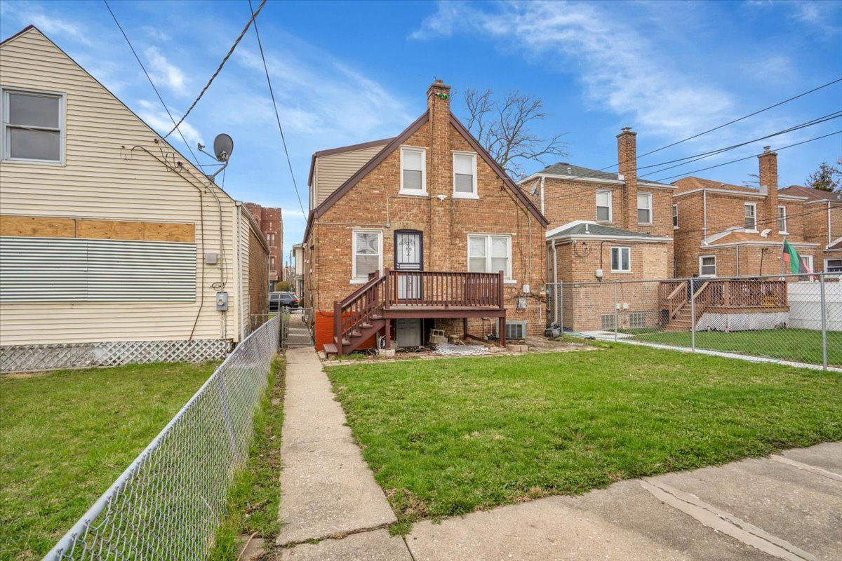 Brick house with a small wooden deck, next to a narrow yard and sidewalk.