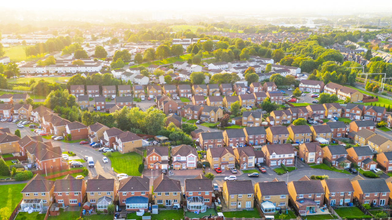 Aerial view of a suburban neighborhood with rows of houses, green trees, and a golden sunset.