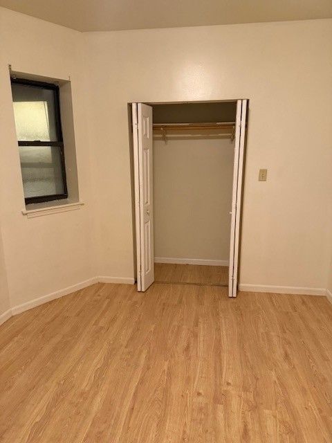 Empty room with wood-look floor, closet, window, and white walls.