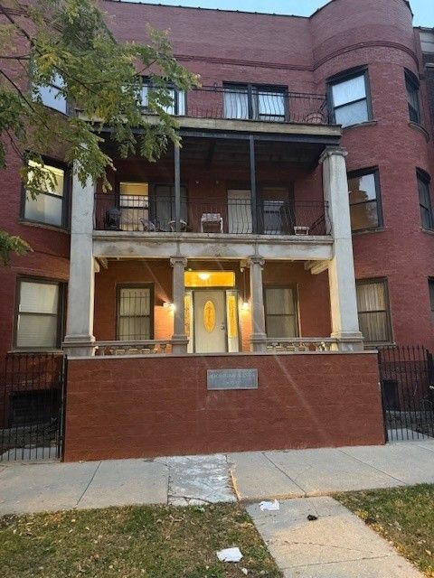 Tan bungalow house with beige roof, bushes, and a small front yard on a sunny day.