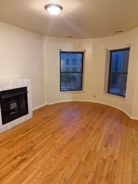Empty living room with hardwood floors, a fireplace, and two windows.