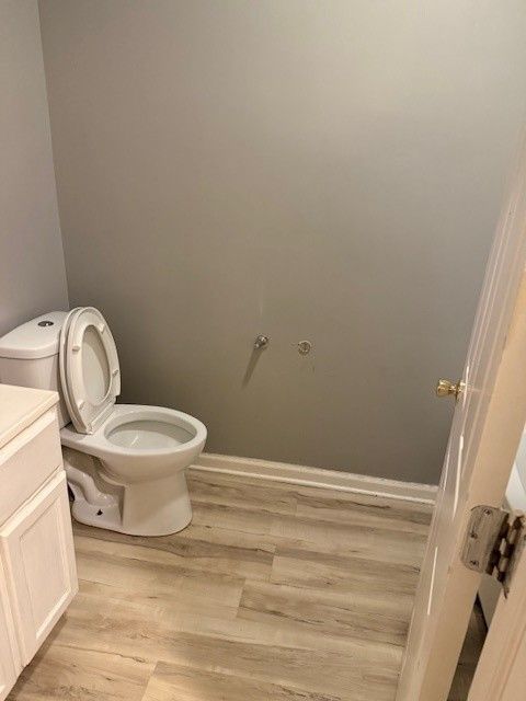 Bathroom with toilet, partially open door, and white vanity, gray walls and light wood-look flooring.