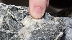 Close-up of a finger pointing at a white vein in a dark gray rock surface
