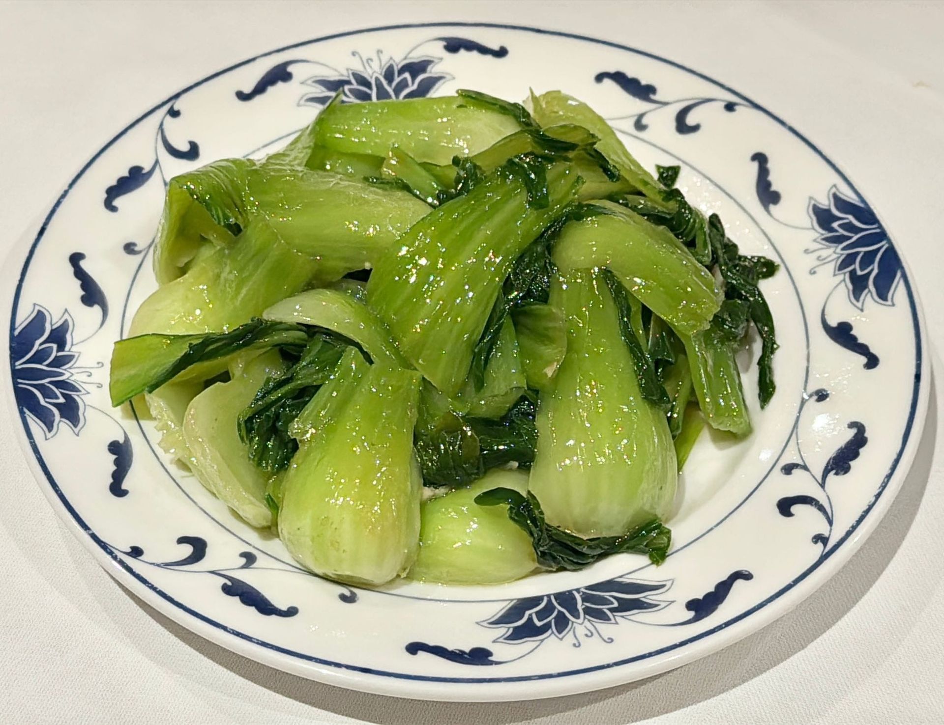 Un piatto bianco con un bordo floreale blu su cui è adagiato un mucchietto di bok choy saltato in padella, di un verde lucido.