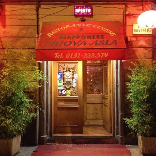 Ingresso del Ristorante Cinese Giapponese Nuova Asia, caratterizzato da una tenda da sole rossa, una porta in legno e piante di bambù in vaso.