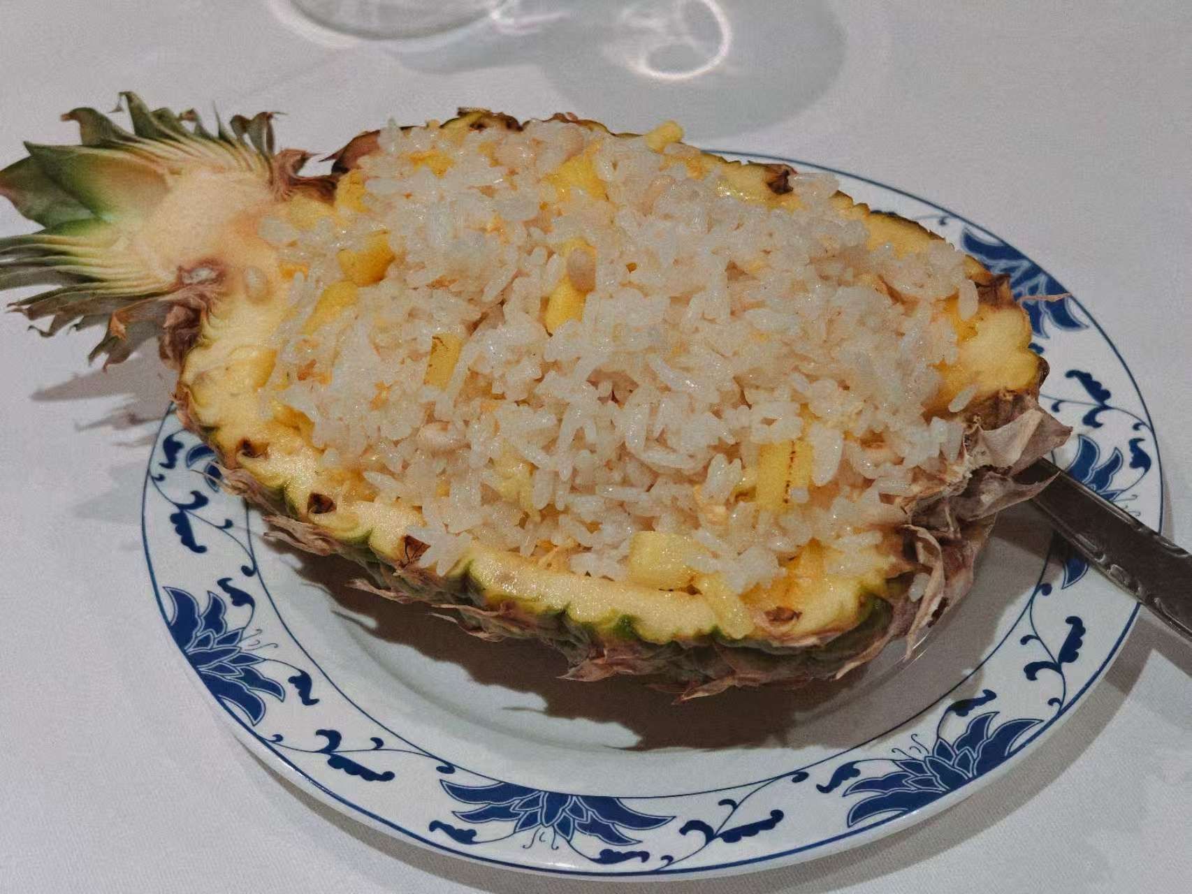 Una porzione di riso fritto all'ananas servita all'interno di una mezza ananas svuotata, adagiata su un piatto con motivo blu e bianco.