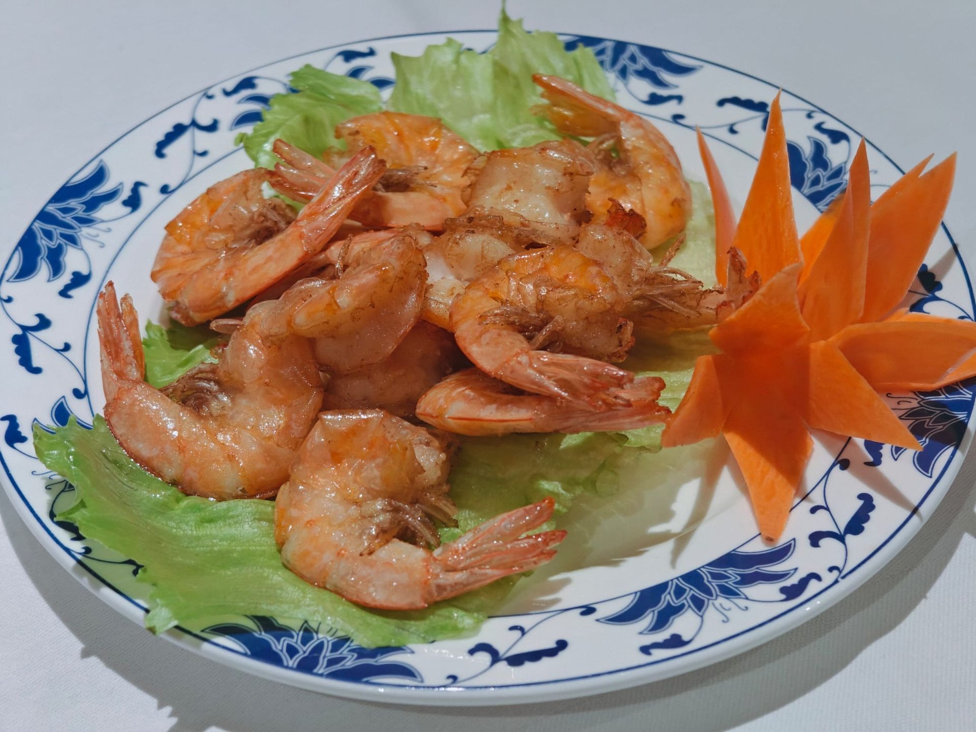 Un piatto di gamberi fritti servito su un letto di lattuga con una guarnizione decorativa di carota intagliata.