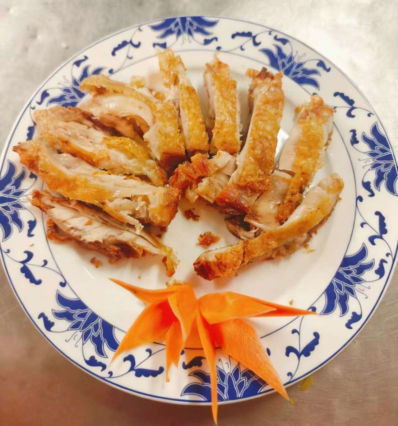 Pollo croccante a fette disposto su un piatto con motivo blu e bianco e guarnito con una carota decorativa.