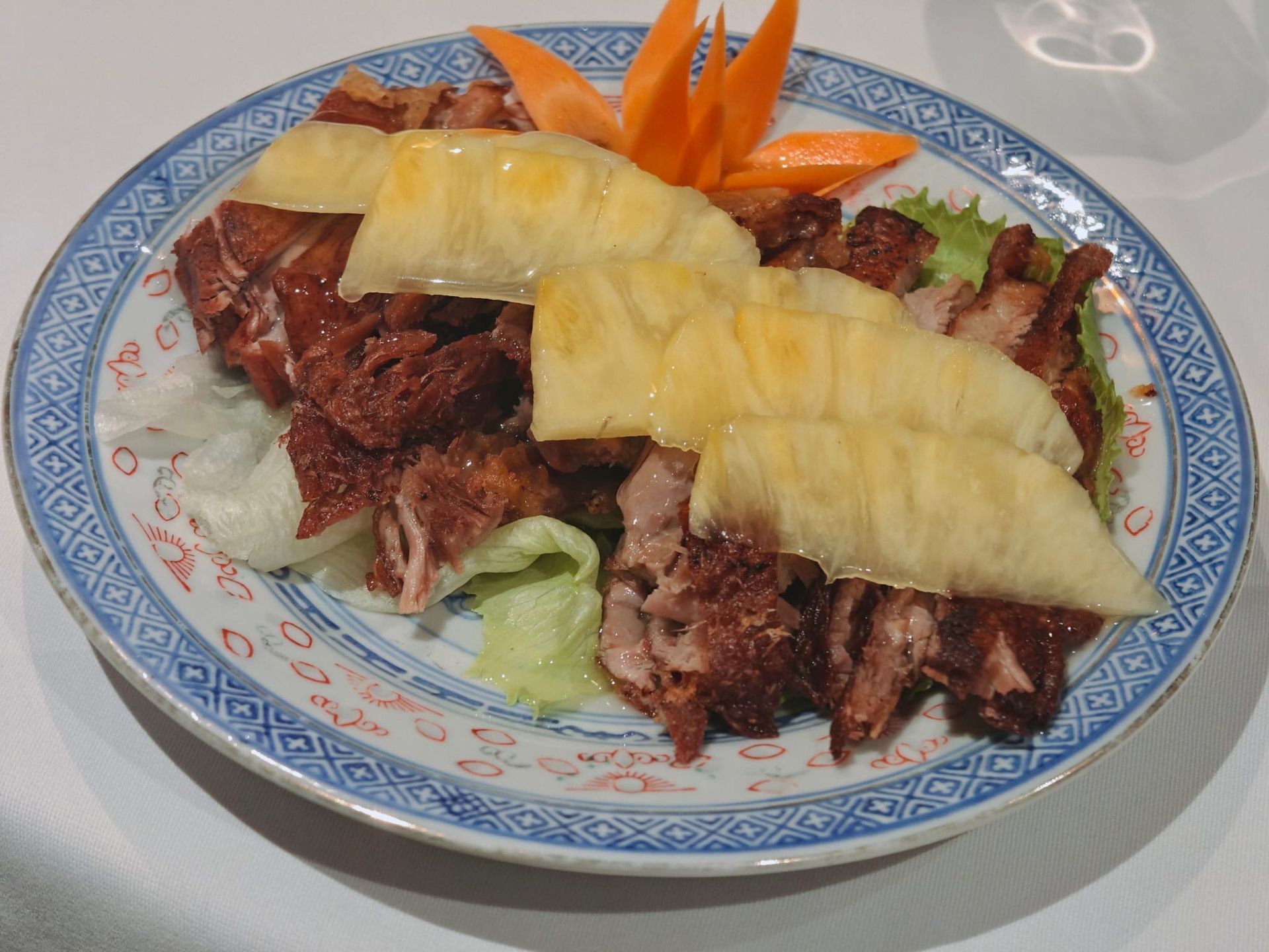 Un piatto di anatra arrosto a fette, guarnita con fette di ananas e una carota, servito su un letto di lattuga.