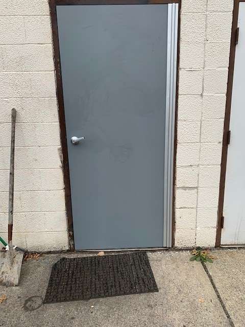A gray door is sitting on a sidewalk next to a brick wall.