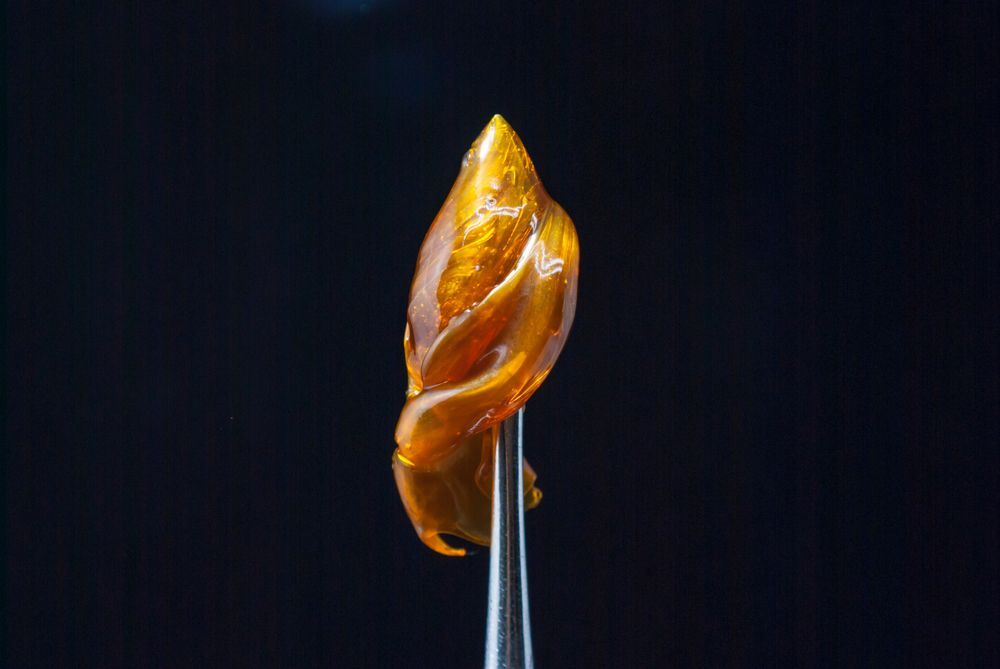 A close up of a piece of wax on a tweezer on a black background.