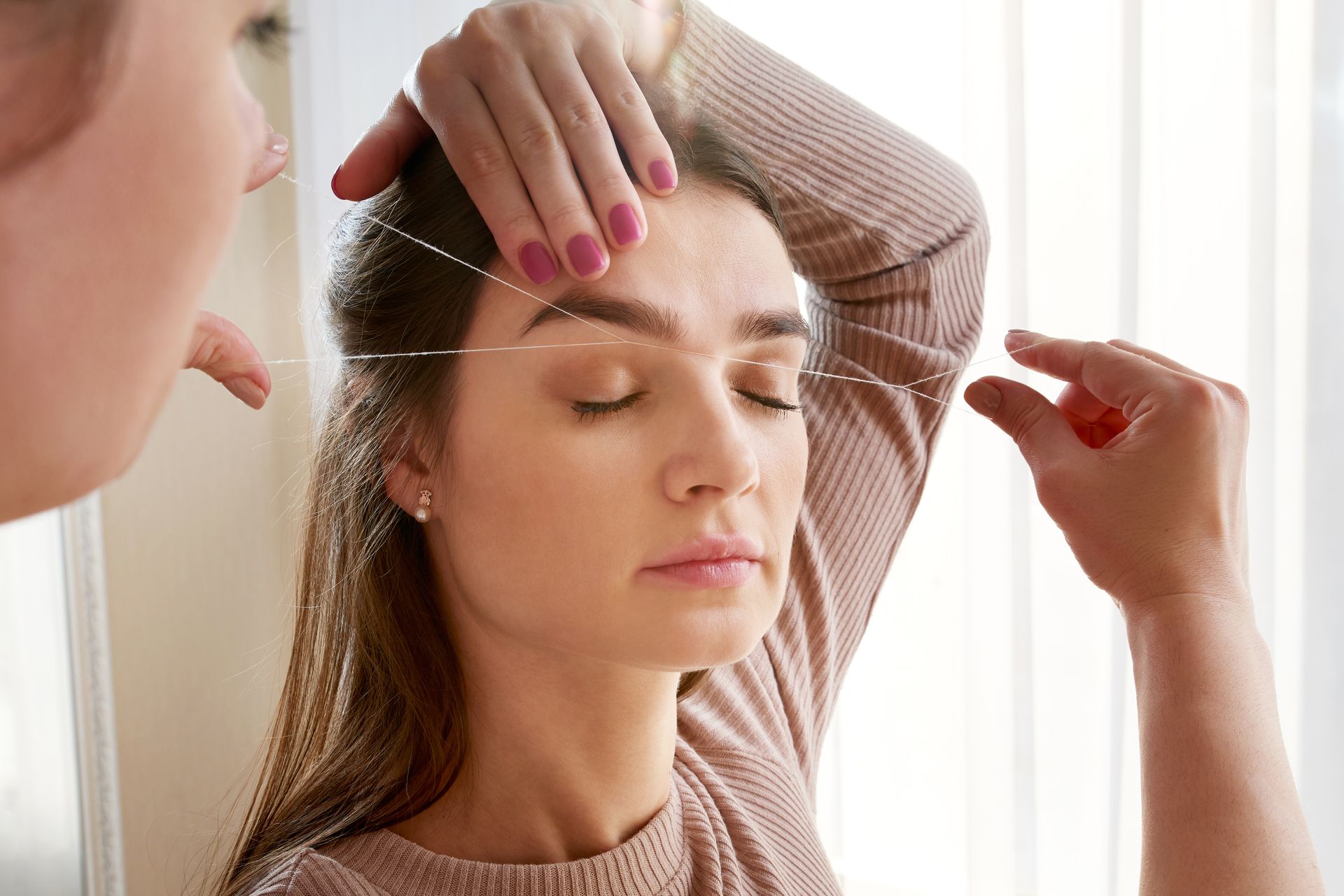 a woman is getting her eyebrows threaded by a man .