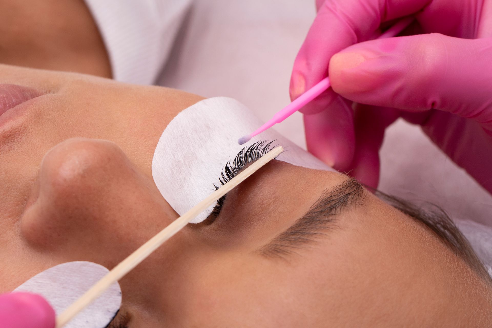 a woman is getting her eyelashes done by a woman wearing pink gloves .