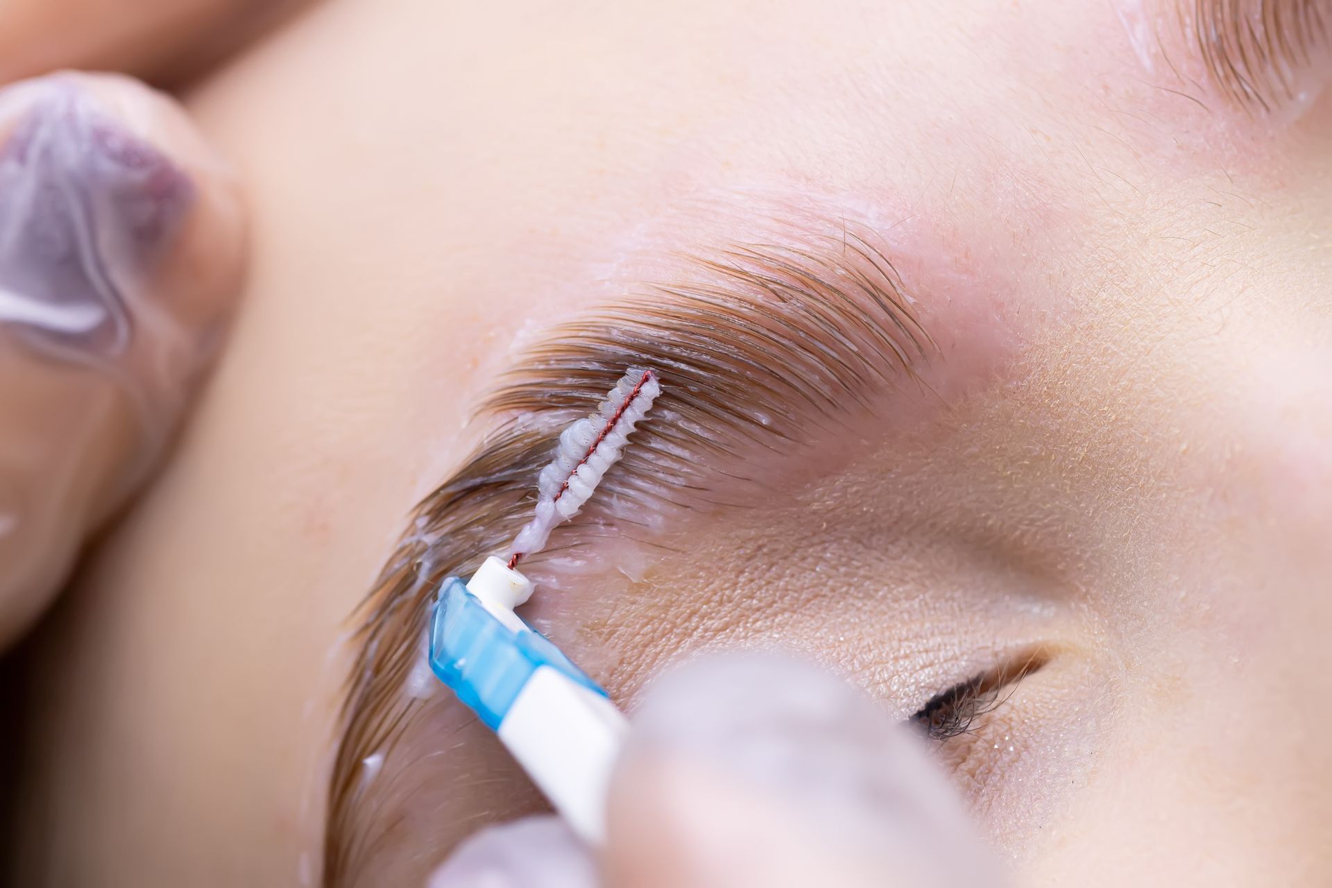 A close up of a person brushing their eyebrows with a toothbrush.