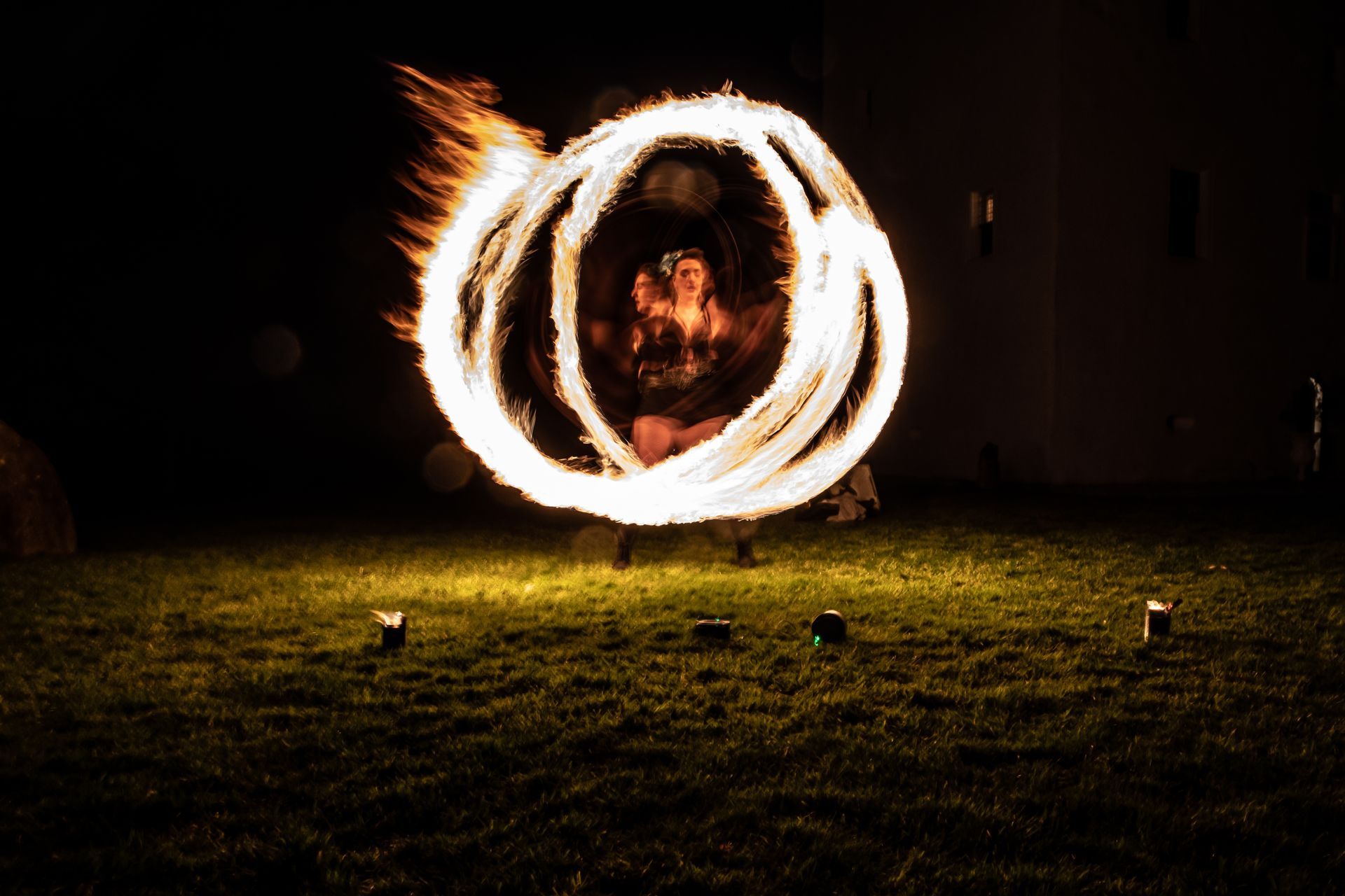 a colour image of Mia Meow stood on some grass in the dark, she is blurred and appears in multiples a long shutter has been used to create multiple fire trails as she spins which appear to surround her in several circles by Lorna Newman Photography