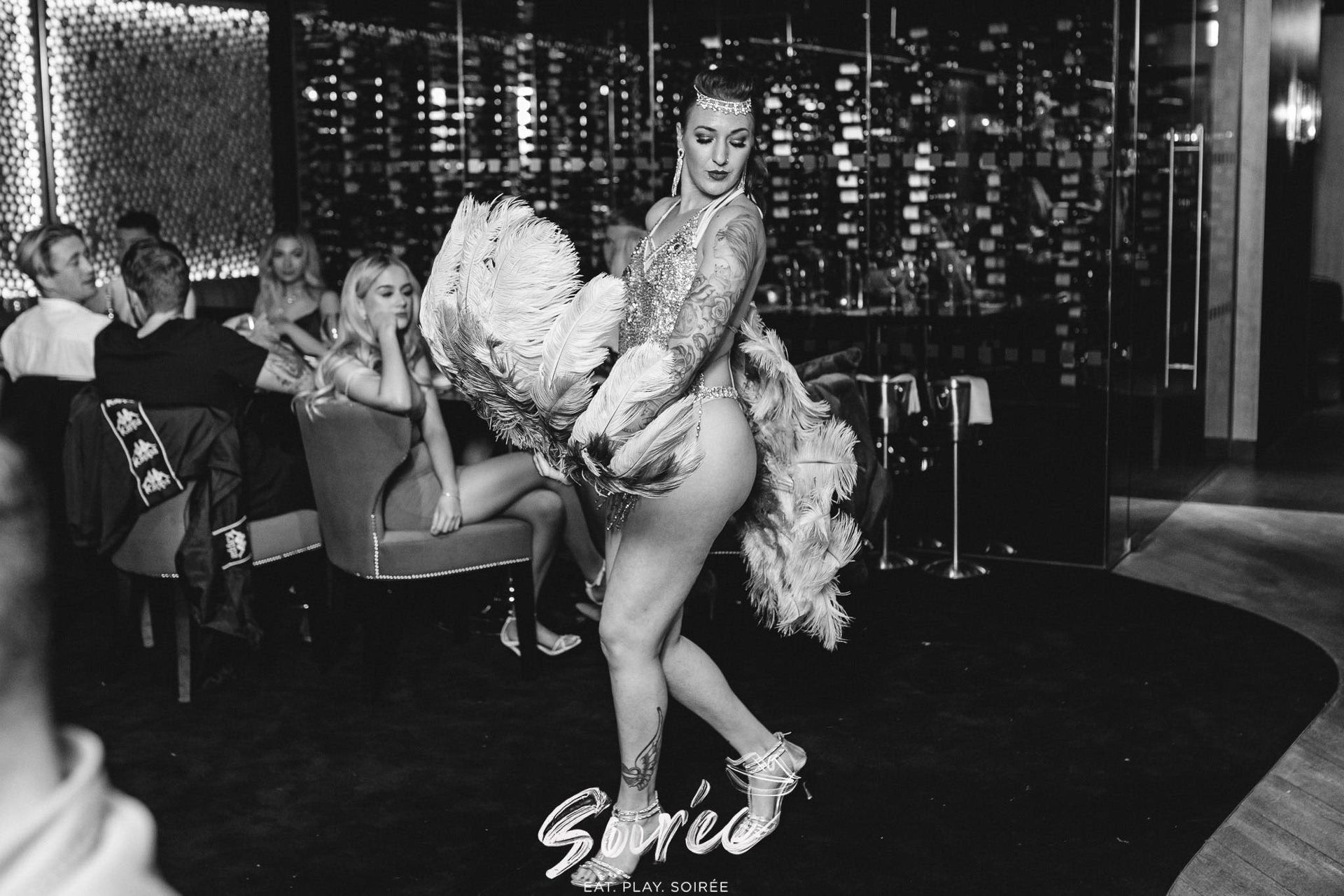 a black and white photo of Mia Meow with feather fans, covering front and back mid-dance by soiree / Devil May Care Agency