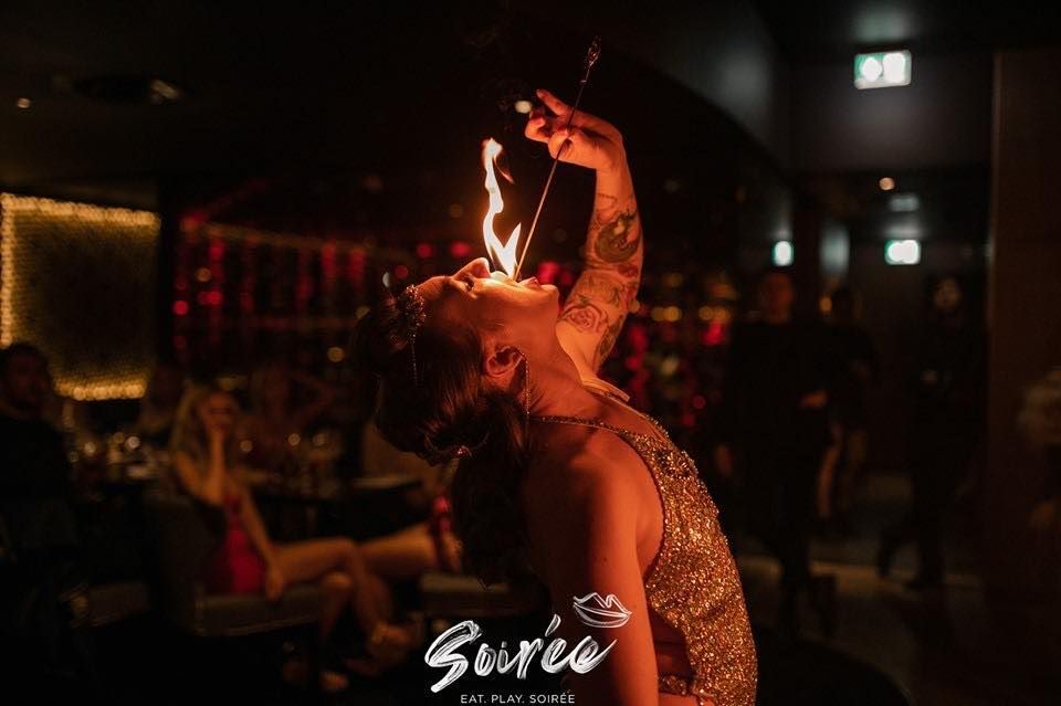 a colour photo of Mia Meow mid fire eating with a flame coming out of her mouth in a cabaret venue by Soiree / Devil May Care Agency