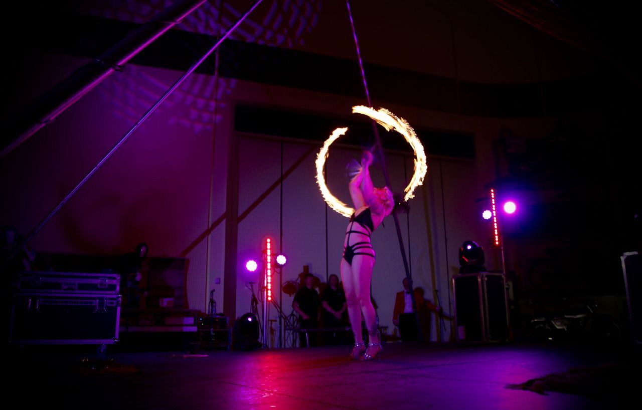 a colour photo of Mia Meow stood on stage, leaning back with her arms above her head, two large fire trails surround her either side from her fire fans by Amy Shipway