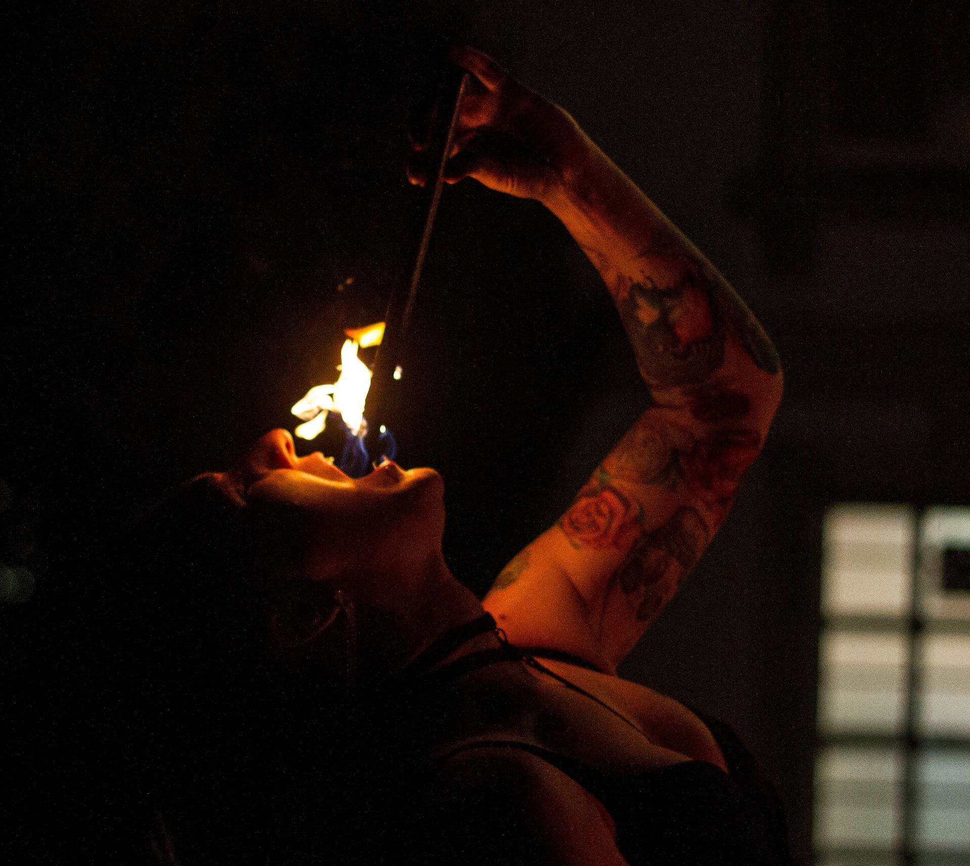 a colour image of Mia Meow from the chest up, with her head back she is mid-fire eat with only the immediate area surrounding her being lit by the flame by Raymond Garrett