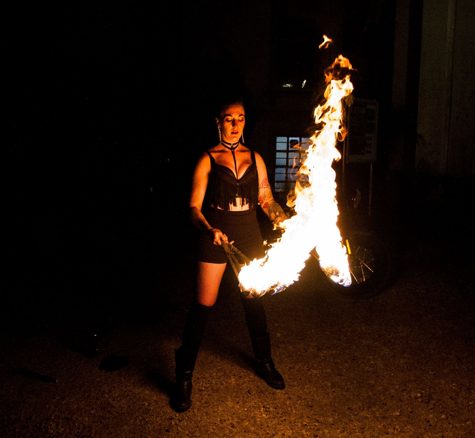 A colour photo of Mia Meow with two large batons of fire with a trail of fire that joins she is looking down at the batons by Raymond Garrett