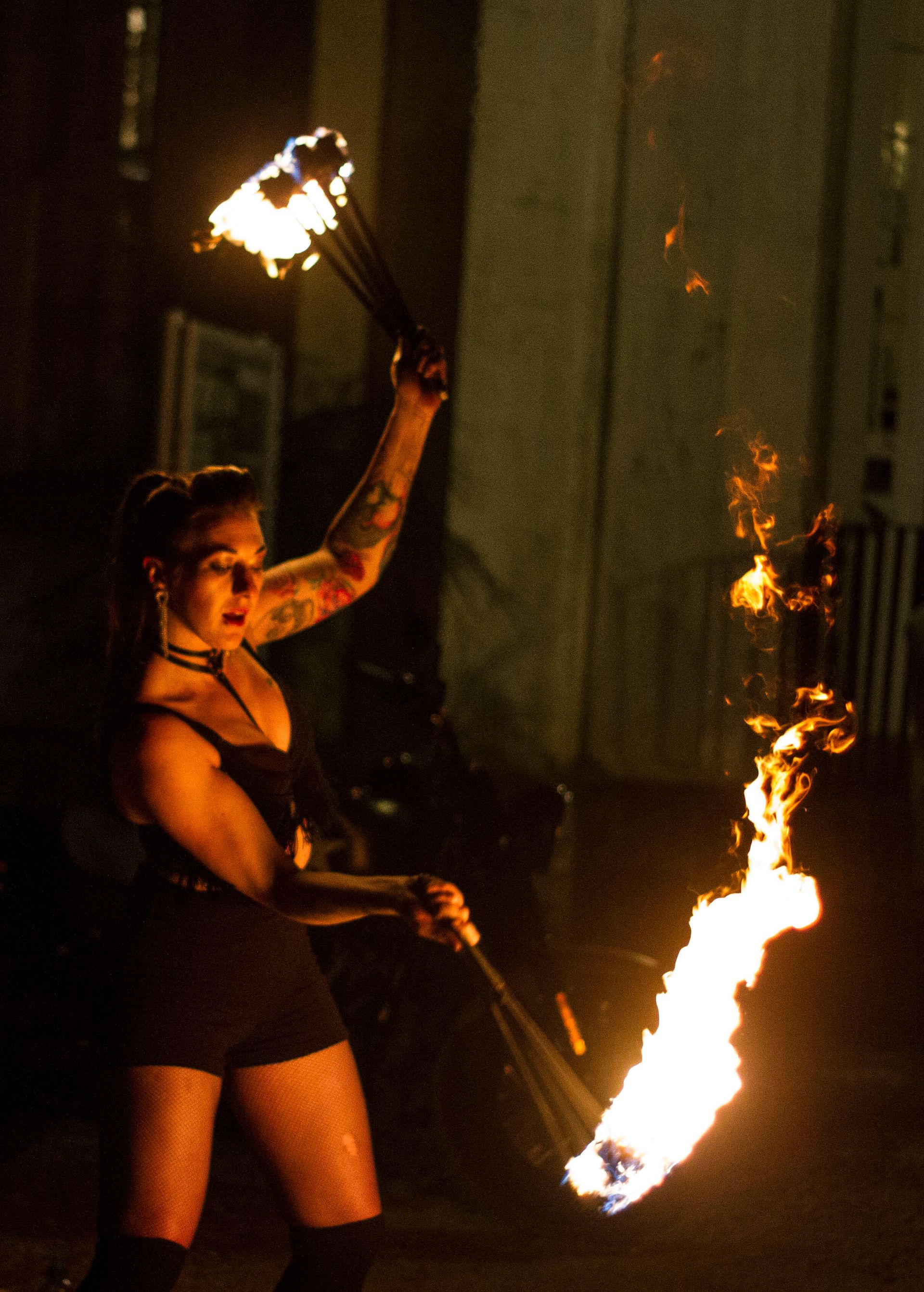 A colour image of Mia Meow with two batons of flames mid-spin with one flame high and the other low, this image is side on by Raymond Garrett