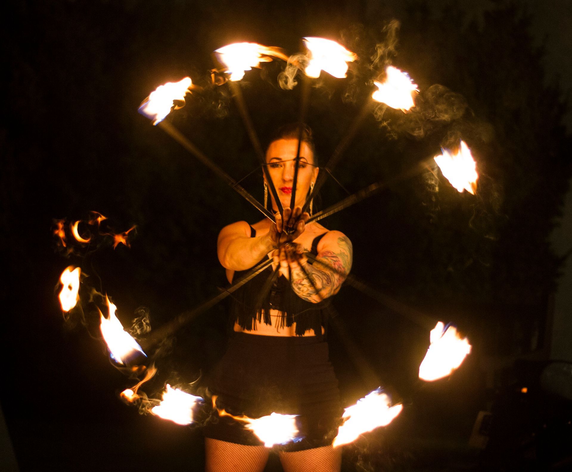 a colour photo of Mia Meow with fire fans held out in front of her with arms stretched forward, the fans create a circle of fire in front by Raymond Garrett