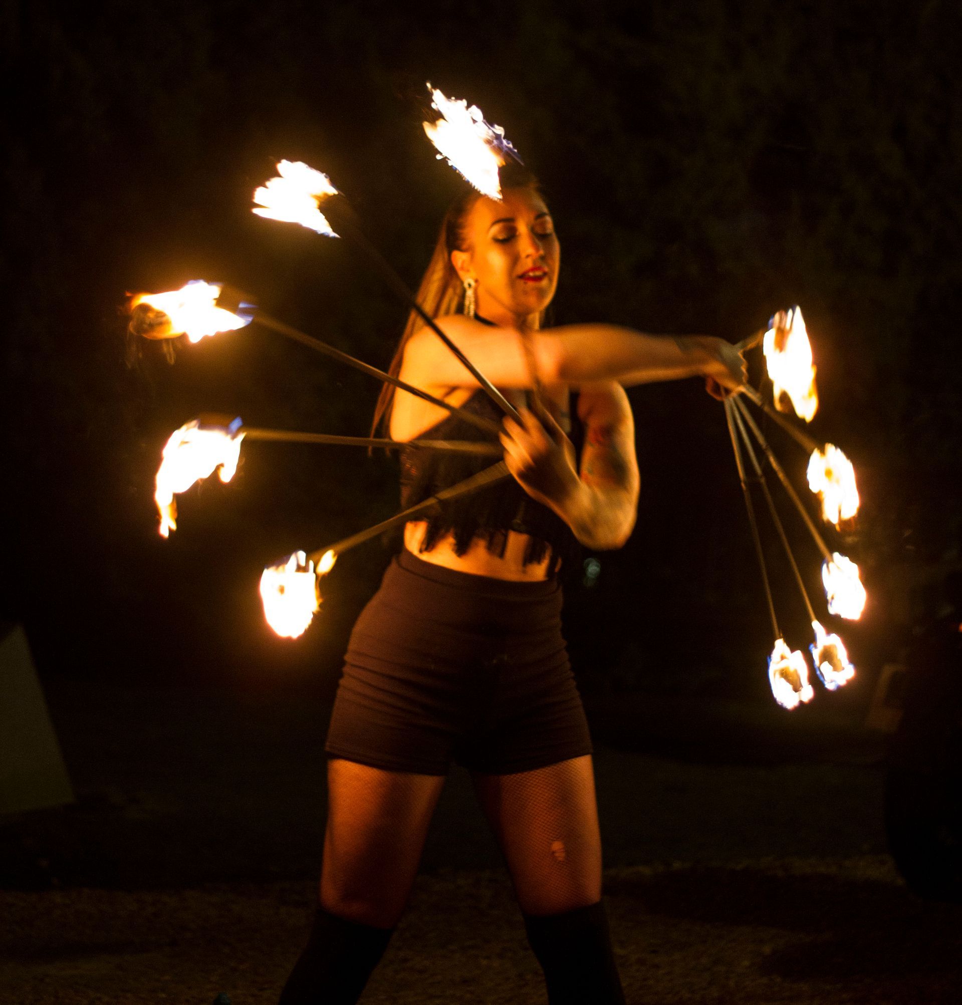 Colour photo of Mia Meow with arms crossed in front holding a splayed fire fan in each hand lit by Raymond Garrett