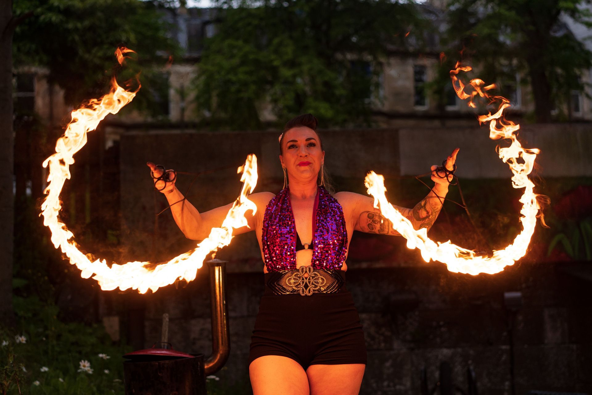 A front on image of Mia Meow with her arms raise to each side, two half moon shape trails are being created by her fire fans and she is looking forwards smiling by Andres McNeill