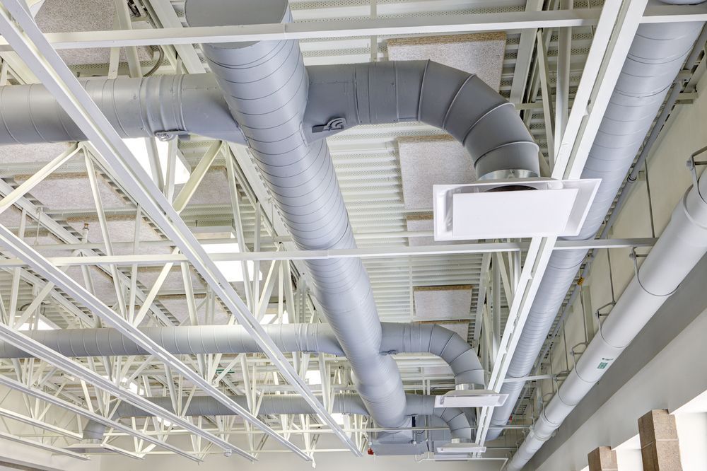 Gray HVAC ductwork against a white ceiling with exposed beams.