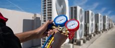 Person using gauges to check air conditioning units on a rooftop.