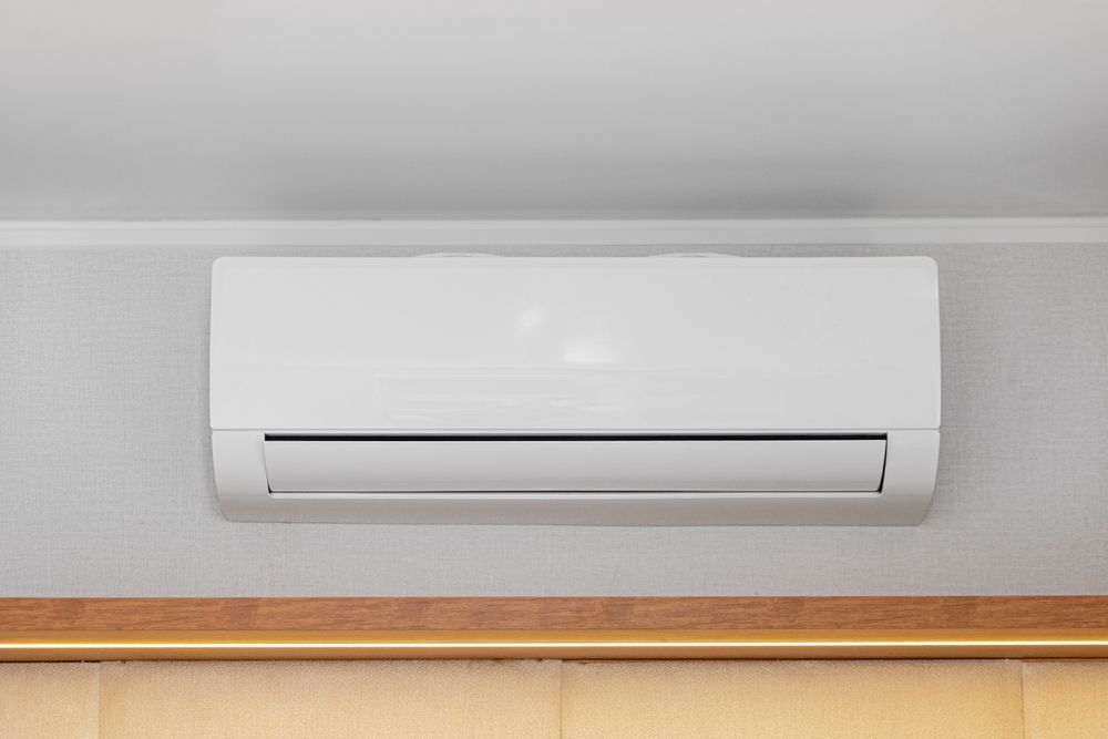 White ductless air conditioner mounted on a gray wall above a wood trim.