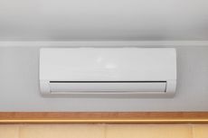 White ductless air conditioner mounted on a gray wall above a wood trim.