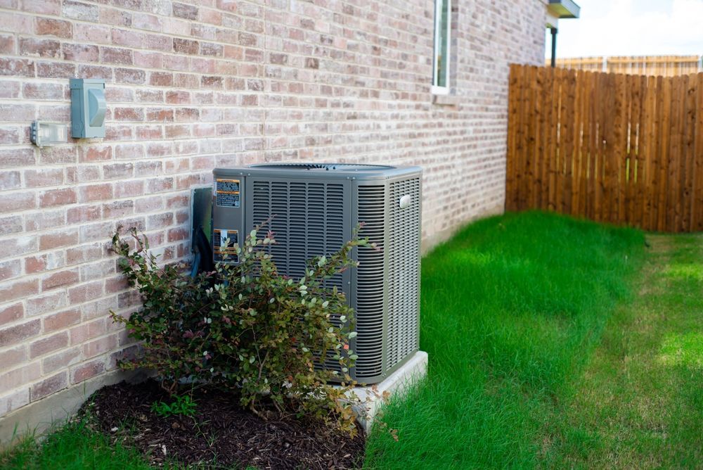 Air conditioner unit next to a brick building and wooden fence, with grass.
